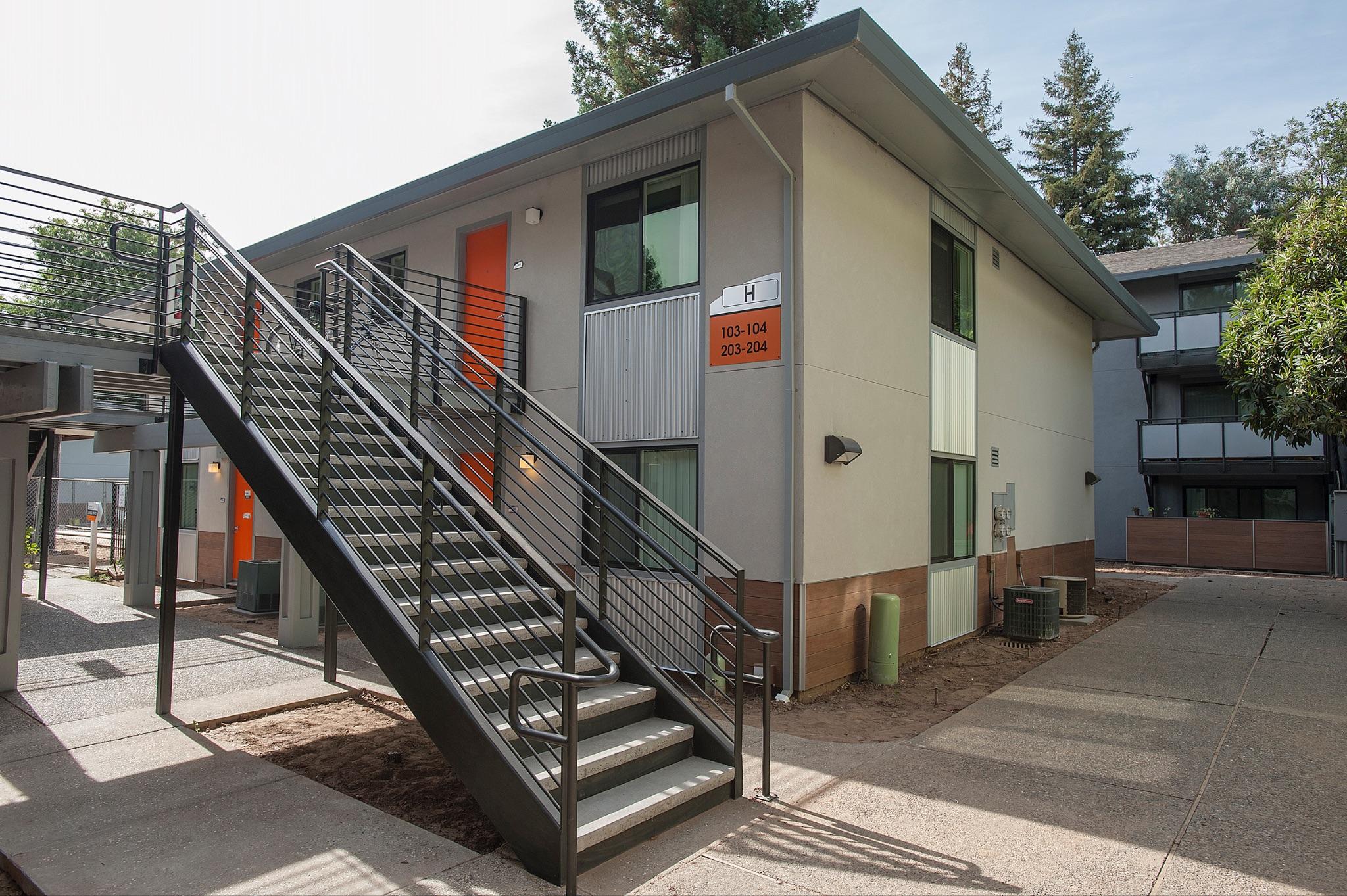 Exterior of two-story apartment building with external staircase and orange doors